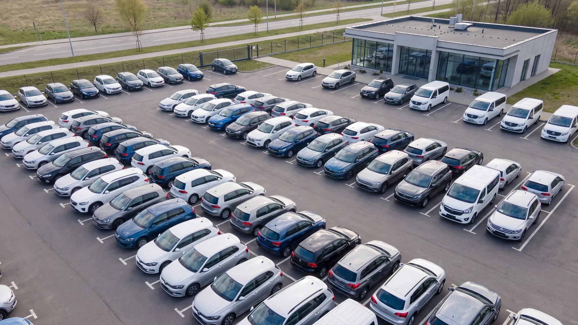Illustration: a car rental lot seen from above, rows of cars of different classes in front of the office.